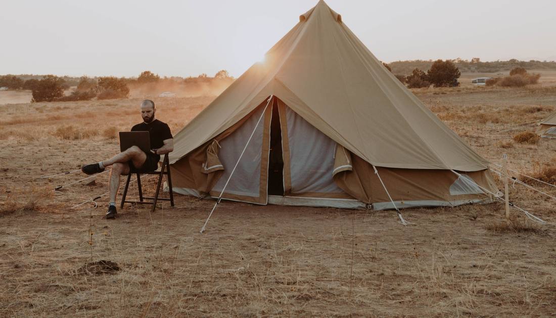 A canvas bell tent pitched alone in open grassland at sunrise
